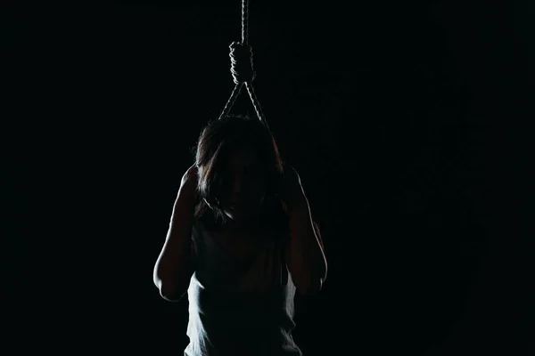 Depressed woman committing suicide while putting noose on neck in darkness isolated on black — Stock Photo