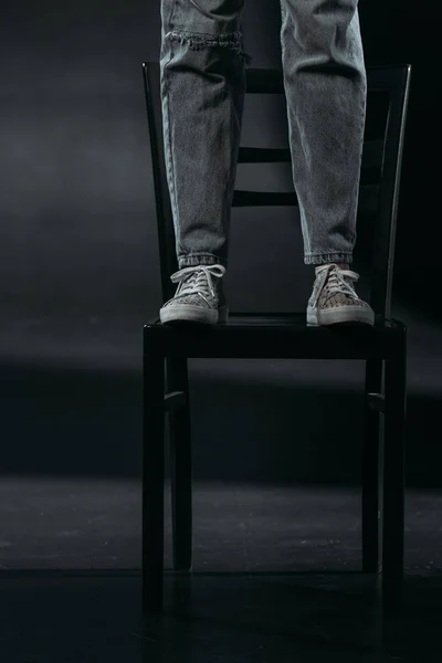 Vista cortada de auto-destruidor em pé na cadeira e vai cometer suicídio em fundo preto — Fotografia de Stock