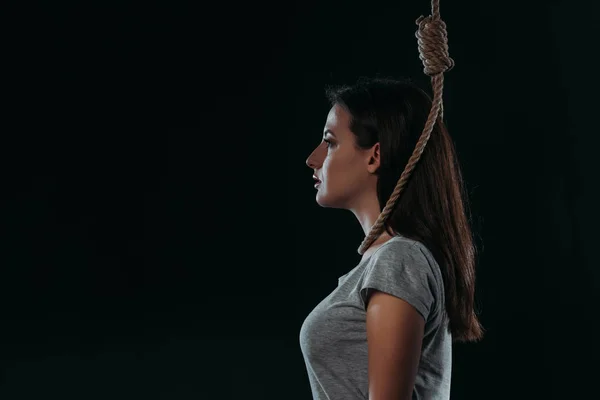 Side view of depressed young woman going to commit suicide by hanging herself isolated on black — Stock Photo