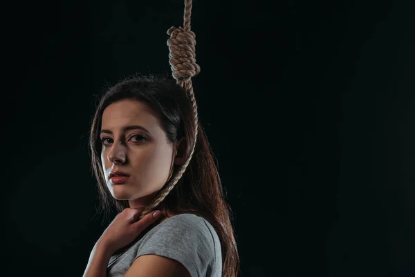Frustrierte junge Frau blickt in die Kamera, während sie mit Schlinge am Hals isoliert auf schwarz steht — Stockfoto