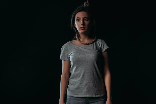 Frustrierte junge Frau schaut weg, während sie mit Schlinge am Hals auf schwarz isoliert steht — Stockfoto