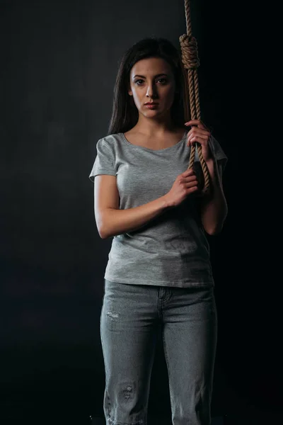 Frustrierte junge Frau blickt in die Kamera, während sie hängende Seilschlinge isoliert auf schwarz hält — Stockfoto