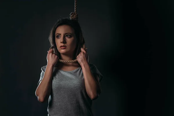 Verzweifelte Frau mit Schlinge am Hals, die vor schwarzem Hintergrund wegschaut — Stockfoto