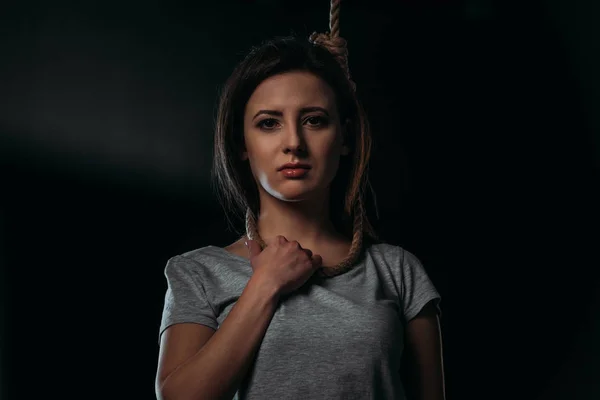 Frustrated woman looking at camera while standing with noose on neck on black background — Stock Photo