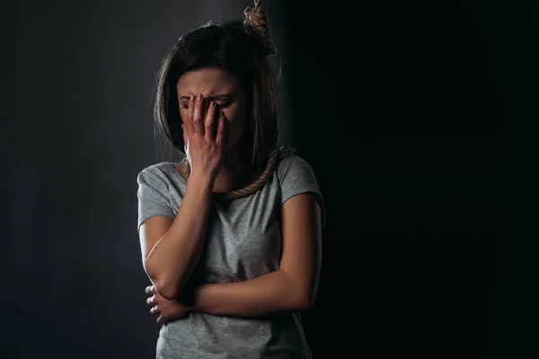 Плачущая женщина, прикрывающая лицо рукой, стоя с петлей на шее на черном фоне — стоковое фото