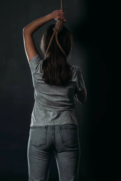 Visão traseira da mulher cometendo suicídio ao colocar laço no pescoço no fundo preto — Fotografia de Stock