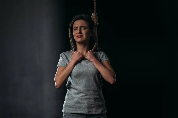 Депрессивная, плачущая женщина, совершающая самоубийство, надевая петлю на шею на черном фоне — стоковое фото