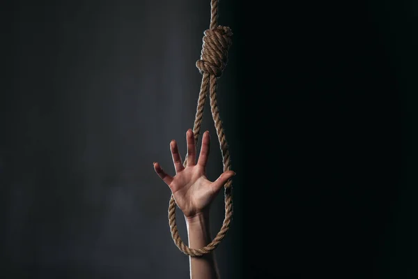 Partial with of female hand in hanging rope noose on black background — Stock Photo