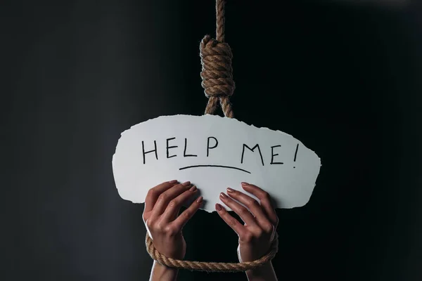 Cropped view of woman holding white paper with help me inscription near hanging noose on black background — Stock Photo