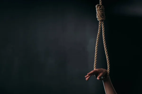 Cropped view of female hand in hanging rope noose on black background — Stock Photo
