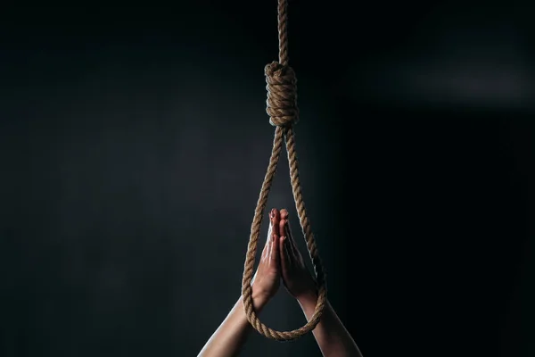 Cropped of woman showing pray gesture near hanging rope noose on black background — Stock Photo