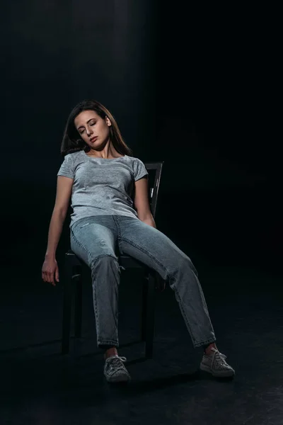 Молодая, безжизненная женщина на стуле после самоубийства на черном фоне — стоковое фото