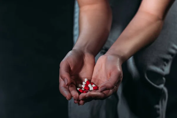Teilbild einer depressiven Frau, die eine Handvoll Tabletten in der Hand hält und isoliert auf schwarz Selbstmord begeht — Stockfoto