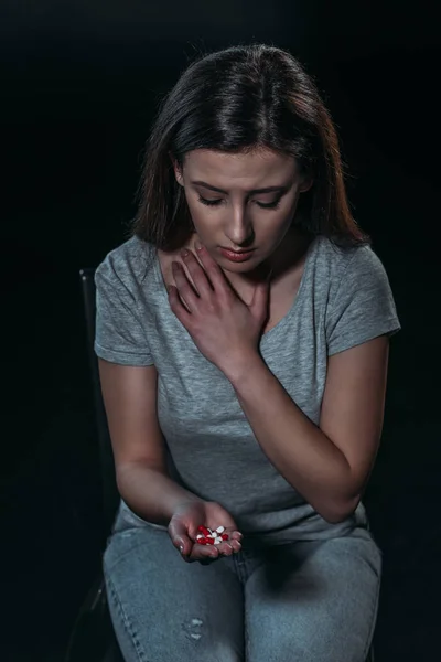 Расстроенная женщина с горсткой таблеток и собирается покончить жизнь самоубийством изолированы на черном — стоковое фото