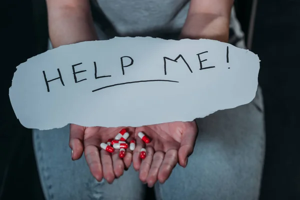 Vista ritagliata della donna con una manciata di pillole e carta con l'aiuto di iscrizione isolato su nero — Foto stock