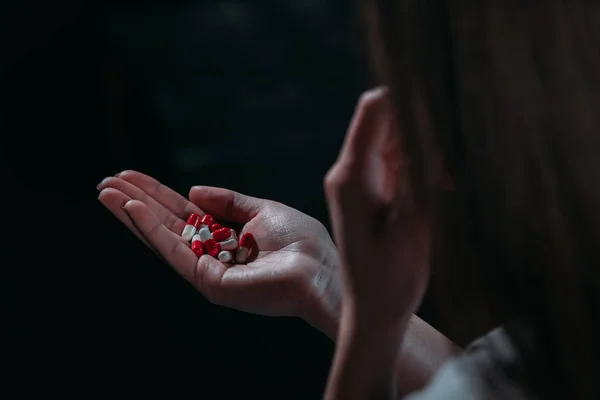 Visão parcial da mulher que vai cometer suicídio e segurando um punhado de pílulas isoladas em preto isolado em preto — Fotografia de Stock