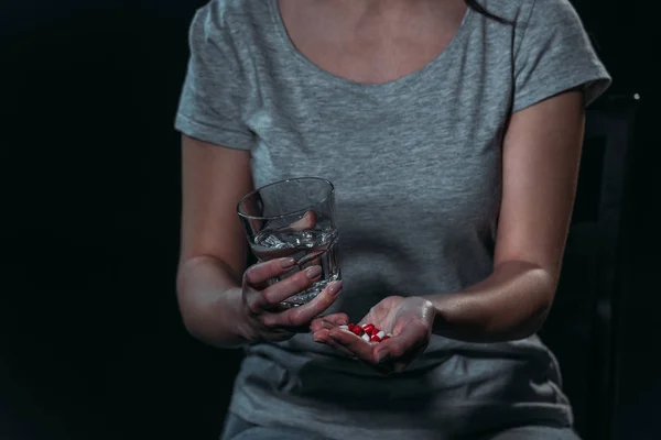 Vue recadrée de la femme va se suicider et tenant une poignée de pilules et un verre d'eau isolé sur noir isolé sur noir — Photo de stock