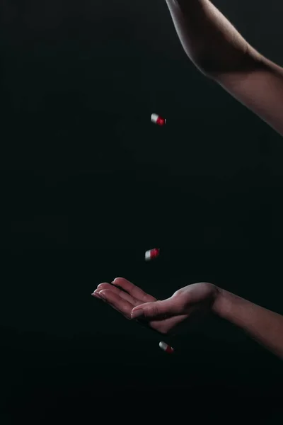 Visão cortada de mulher jogando pílulas na mão aberta enquanto vai cometer suicídio isolado no preto — Fotografia de Stock