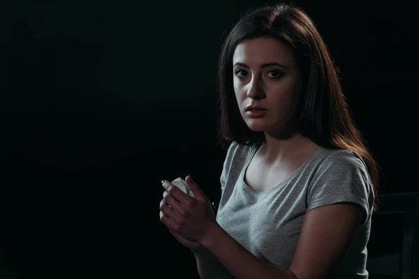 Mujer frustrada mirando a la cámara mientras se va a suicidar y sosteniendo contenedor con pastillas aisladas en negro - foto de stock