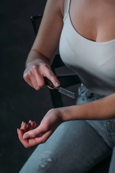 Partial view of woman committing suicide by cutting veins with straight razor on dark background — Stock Photo
