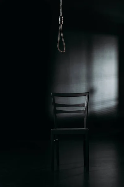 Стул под петлей веревки на черном фоне с освещением, концепция предотвращения самоубийства — стоковое фото
