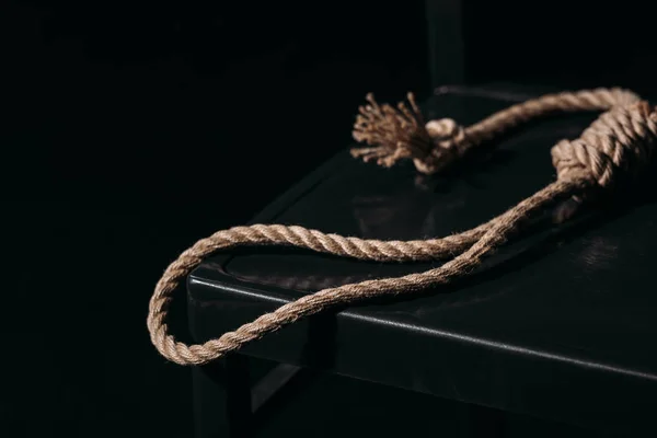 Rope noose on chair on black background, suicide prevention concept — Stock Photo