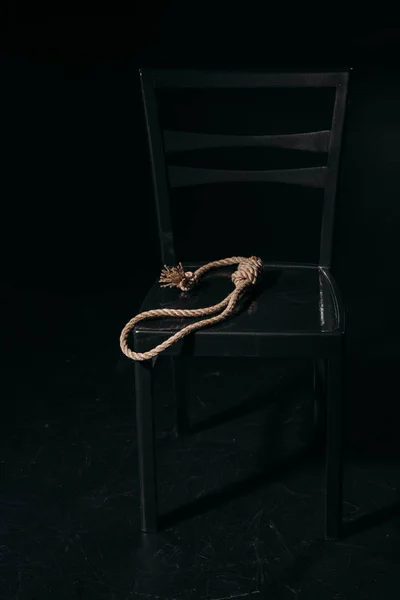 Seilschlinge auf Stuhl auf schwarzem Hintergrund, Suizidpräventionskonzept — Stockfoto