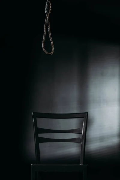 Stuhl unter hängender Seilschlinge auf schwarzem Hintergrund mit Beleuchtung, Suizidpräventionskonzept — Stockfoto