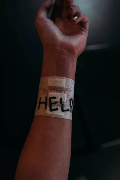 Обрезанный вид женской руки со словом помощи на медицинских участках покрывающих разрезы вен на черном фоне — стоковое фото