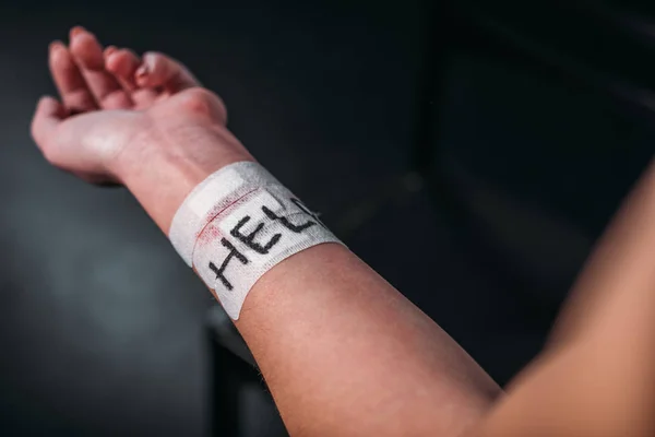 Partial view of woman showing hand with word help on medical patches fixed on cut wrist on black background — Stock Photo