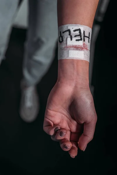 Partial view of woman showing hand with word help on medical patches covering cut veins on black background — Stock Photo