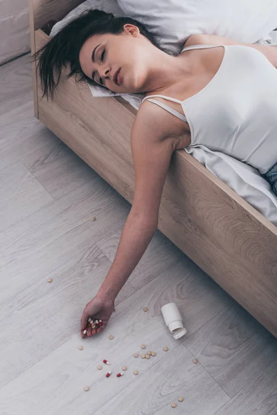 Unconscious woman, committed suicide by overdosing medicines, lying on bed near container with pills — Stock Photo