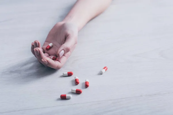 Ausgeschnittene Ansicht einer leblosen Frau, die durch Überdosierung von Medikamenten Selbstmord beging, auf dem Boden liegend in der Nähe verstreuter Tabletten — Stockfoto