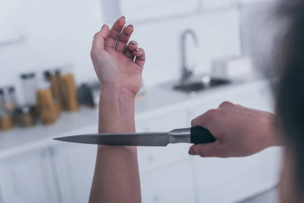 Partial view of depressed woman committing suicide by cutting veins with knife in kitchen — Stock Photo