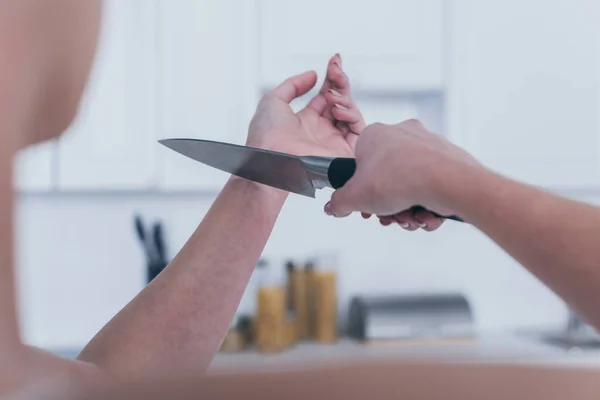 Cropped view of depressed woman committing suicide by cutting veins with knife in kitchen — Stock Photo