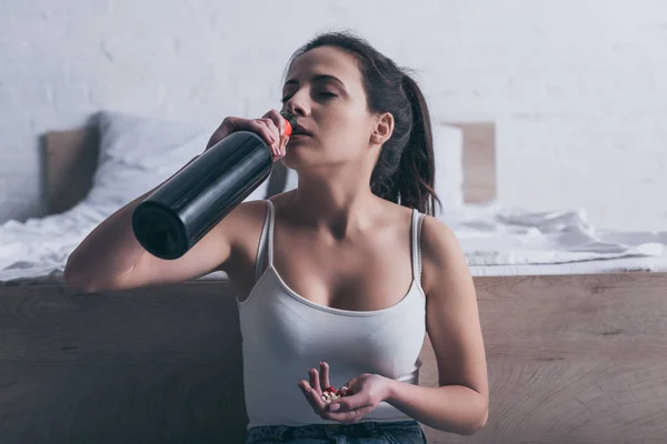 Депрессивная молодая женщина пьет алкоголь и собирается покончить жизнь самоубийством при передозировке лекарств — стоковое фото