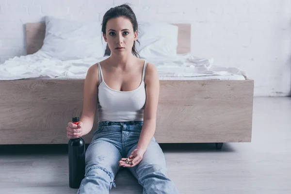 Disperata giovane donna seduta sul pavimento con una bottiglia di alcol e andare a suicidarsi da farmaci overdose — Foto stock