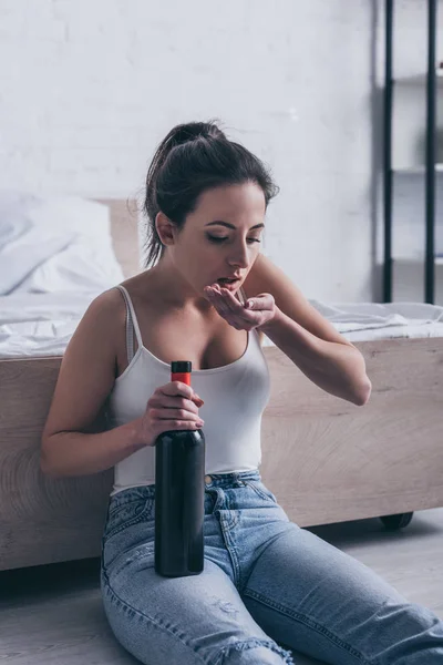 Depressed young woman sitting on floor with bottle of alcohol and committing suicide by overdosing medicines — Stock Photo