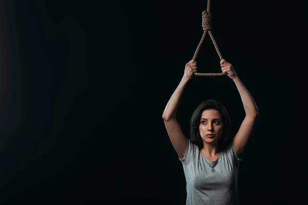 Занепокоєна молода жінка збирається покінчити життя самогубством, тримаючи висячу мотузку ізольовану на чорному — стокове фото