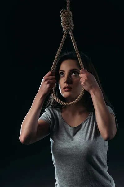 Frustrated young woman committing suicide while putting hanging rope noose on head isolated on black — Stock Photo