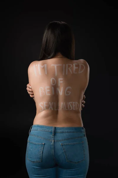 Back view of plus size model with lettering I 'm tired of Being Sexualised on naked back isolated on black — стоковое фото