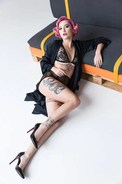 Соблазнительная татуированная девушка в прозрачном нижнем белье позирует на диване — стоковое фото