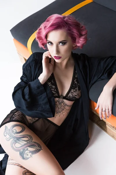 Соблазнительная татуированная девушка в прозрачном нижнем белье позирует на диване — стоковое фото