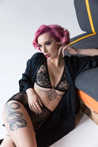 Seductive tattoed pink haired girl in transparent lingerie posing at couch — Stock Photo