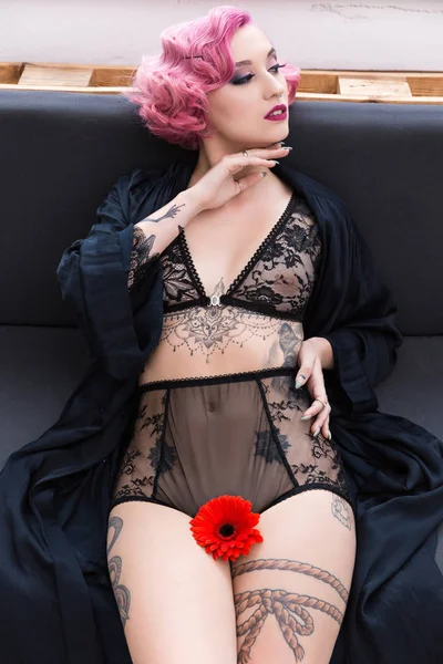 Sexy mujer joven en ropa interior negra con tatuajes y flor roja - foto de stock