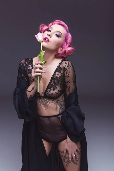 Séduisante pin up girl en lingerie transparente avec fleur devant fond gris — Photo de stock