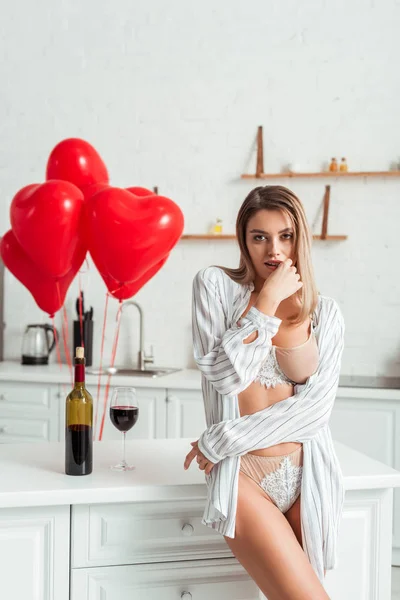 Donna seducente in piedi vicino bottiglia con vino rosso e palloncini a forma di cuore — Foto stock