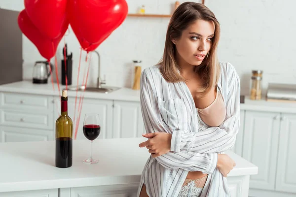Mujer sexy con gran pecho de pie cerca de la botella con vino tinto y globos en forma de corazón - foto de stock