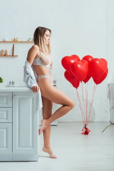 Вид сбоку соблазнительной девушки с большой грудью, стоящей рядом с воздушными шарами в форме сердца — стоковое фото